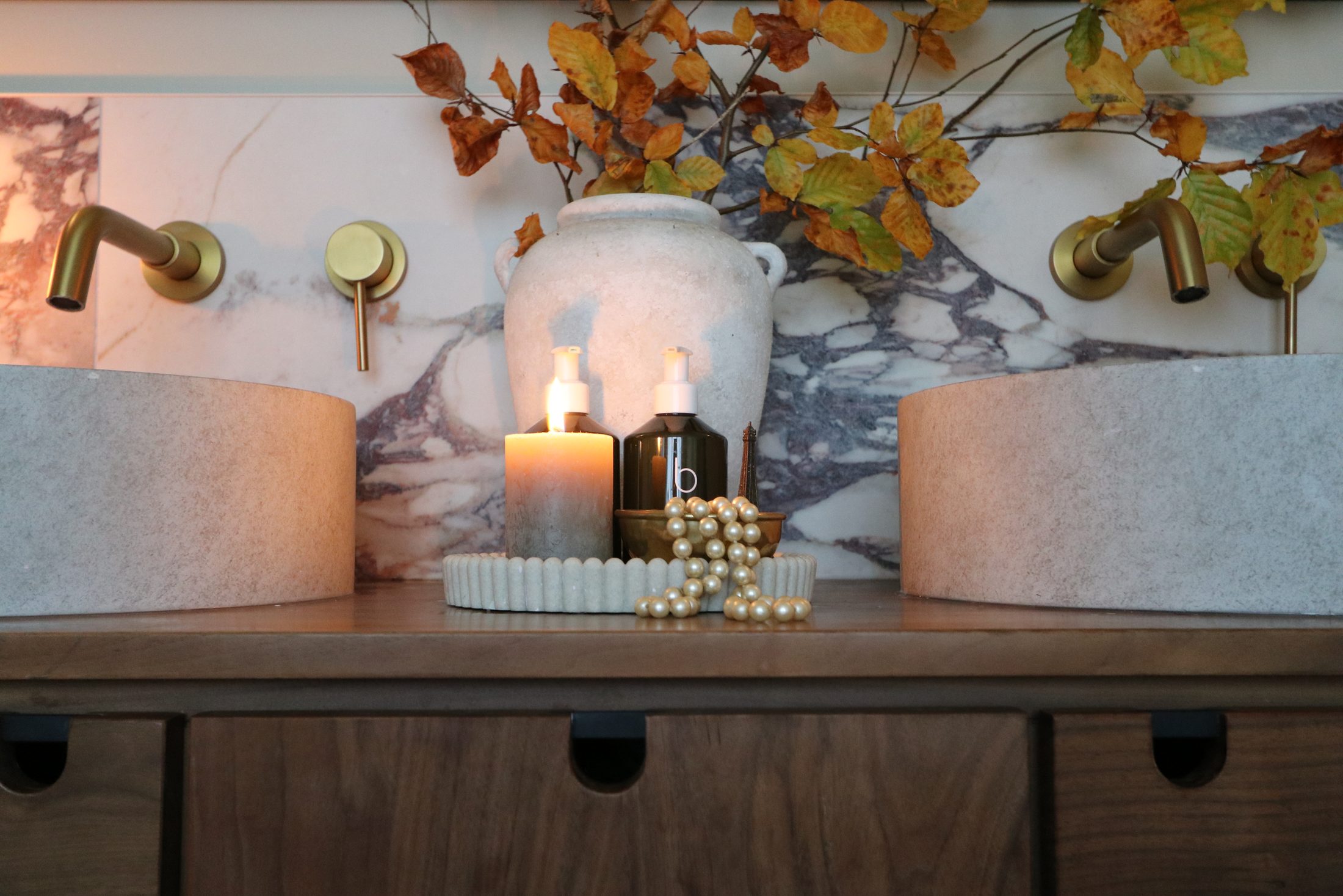 Double stone basins on a walnut vanity, brass taps against Calacatta Viola marble, with autumn beech branches